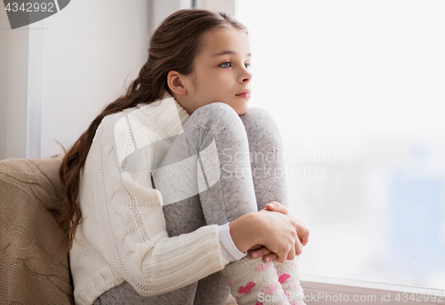 Image of sad girl sitting on sill at home window in winter