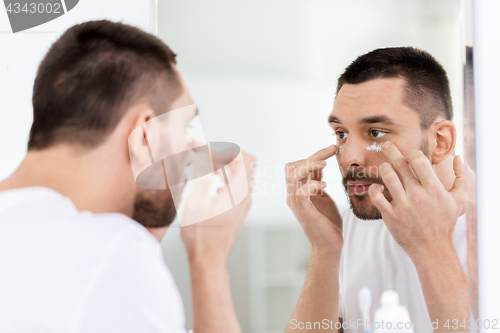 Image of young man applying cream to face at bathroom