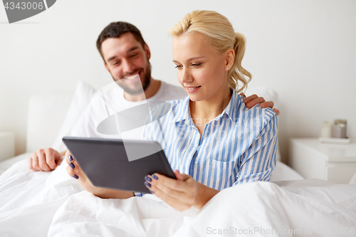 Image of smiling happy couple with tablet pc in bed at home