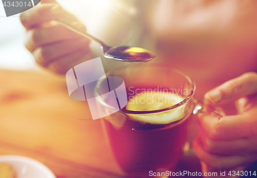 Image of close up of woman adding honey to tea with lemon