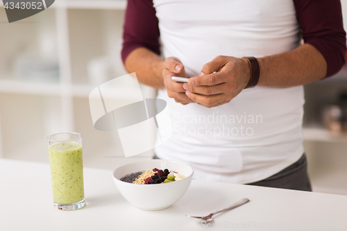 Image of man with smartphone having breakfast at home