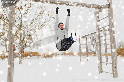 Image of young man exercising on horizontal bar in winter