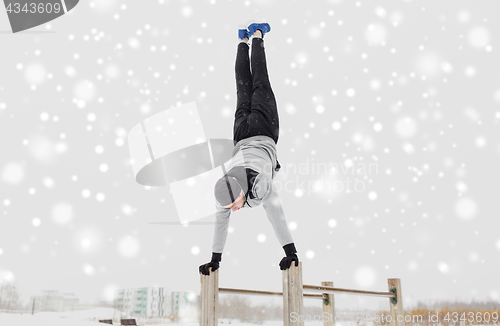 Image of young man exercising on parallel bars in winter