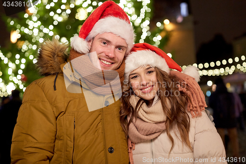 Image of happy couple in santa hats at christmas tree