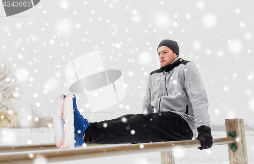 Image of young man exercising on parallel bars in winter