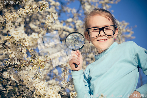 Image of Happy little girl exploring nature with magnifying glass at the 