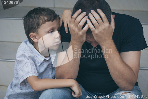 Image of Portrait of young sad little boy and father sitting outdoors at 