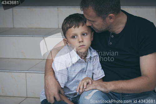 Image of Portrait of young sad little boy and father sitting outdoors at 