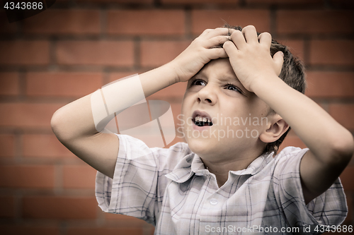 Image of portrait one sad little boy standing near a wall  at the day tim