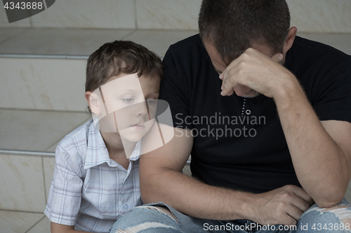 Image of Portrait of young sad little boy and father sitting outdoors at 