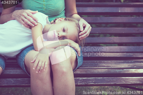 Image of Sad mother and daughter sitting on bench in the park