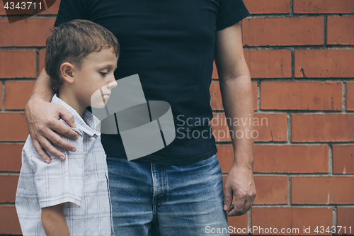 Image of Portrait of young sad little boy and father sitting outdoors at 