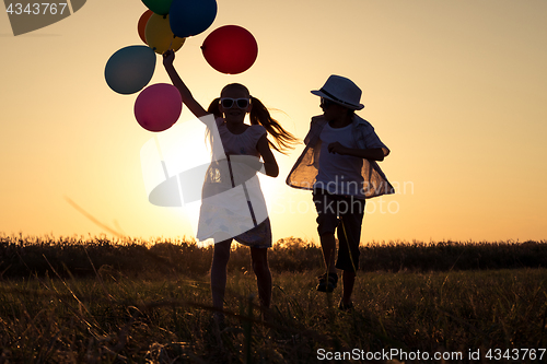 Image of Silhouette of two happy children which playing on the field at t