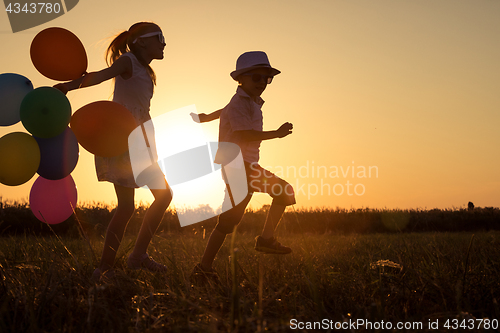 Image of Silhouette of two happy children which playing on the field at t