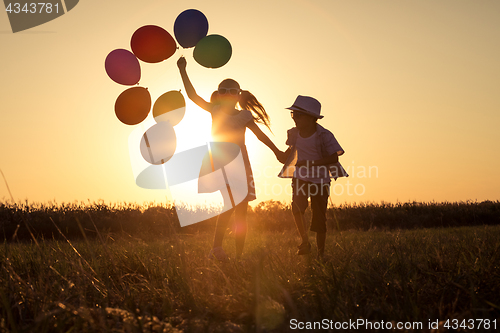 Image of Silhouette of two happy children which playing on the field at t