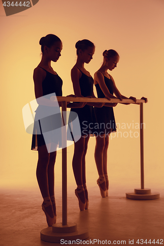 Image of Composition from silhouettes of three young dancers in ballet poses on a orange background.