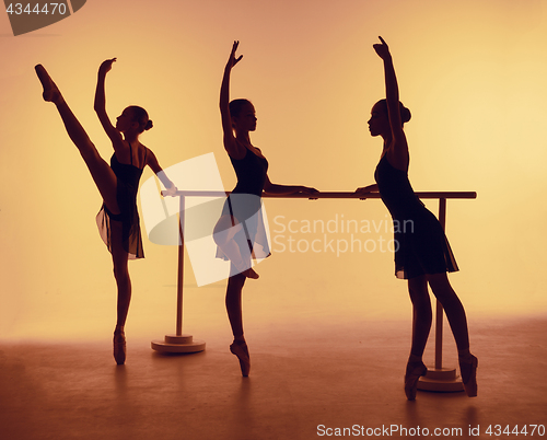 Image of Composition from silhouettes of three young dancers in ballet poses on a orange background.