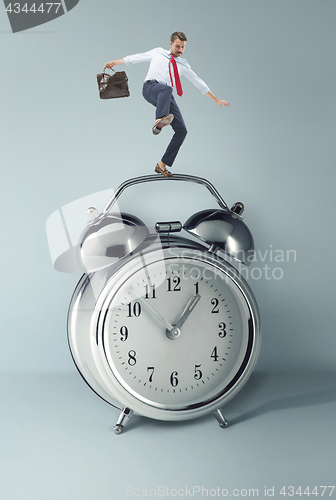 Image of Businessman balancing over alarm clock.