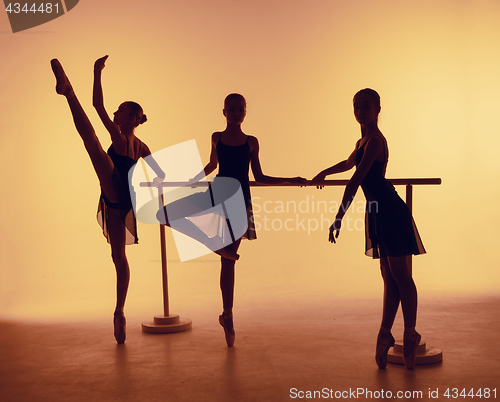 Image of Composition from silhouettes of three young dancers in ballet poses on a orange background.