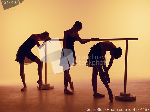 Image of Composition from silhouettes of three young dancers in ballet poses on a orange background.