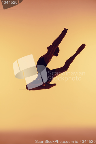 Image of Beautiful young ballet dancer jumping on a orange background.