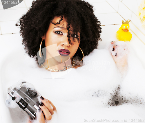 Image of young afro-american teen girl laying in bath with foam, wearing 