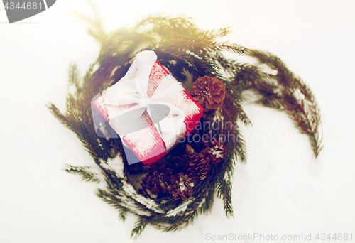 Image of christmas gift and fir wreath with cones on snow