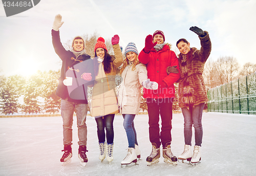 Image of happy friends ice skating on rink outdoors