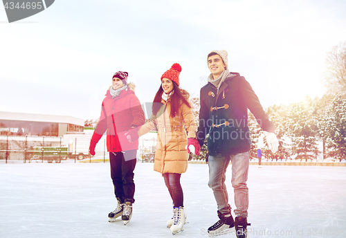 Image of happy friends ice skating on rink outdoors