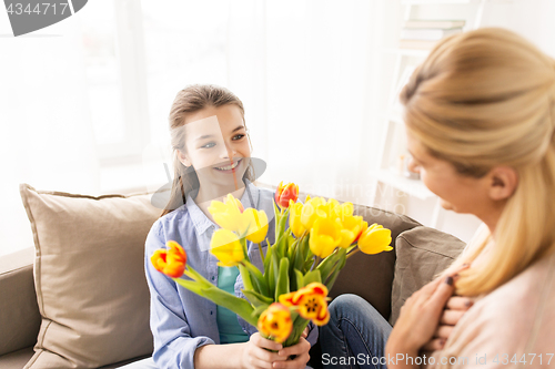 Image of happy girl giving flowers to mother at home