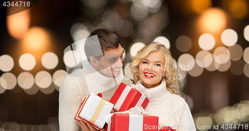 Image of happy couple in sweaters holding christmas gifts