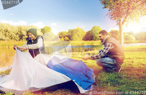 Image of happy father and son setting up tent outdoors