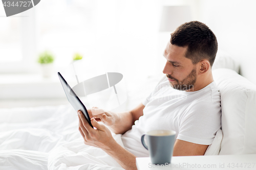 Image of young man with tablet pc in bed at home bedroom