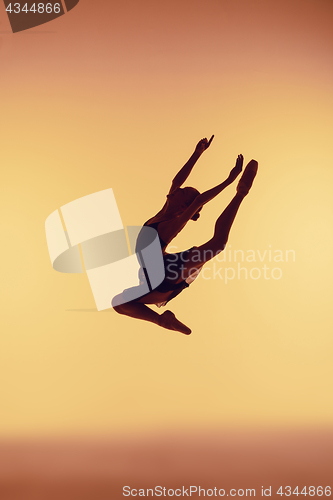 Image of Beautiful young ballet dancer jumping on a orange background.