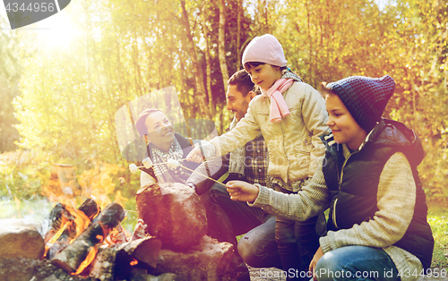 Image of happy family roasting marshmallow over campfire