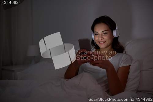 Image of woman with smartphone and headphones in bed