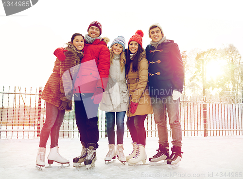 Image of happy friends ice skating on rink outdoors