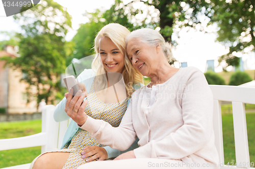 Image of daughter and senior mother with smartphone at park