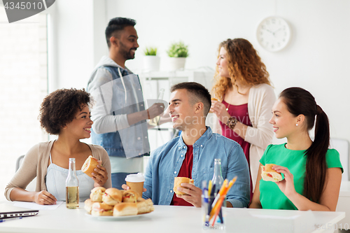 Image of happy friends or team eating at office party