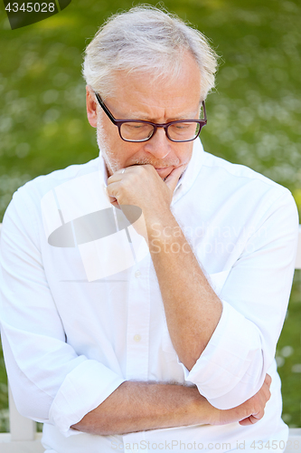 Image of thoughtful senior man sitting at summer park