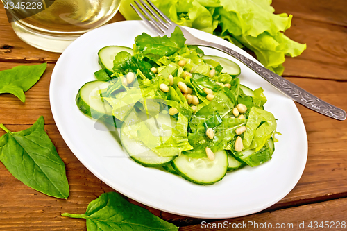 Image of Salad from spinach and cucumber with fork on wooden board