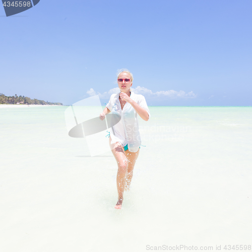 Image of Young active woman having fun running and splashing in shellow sea water.