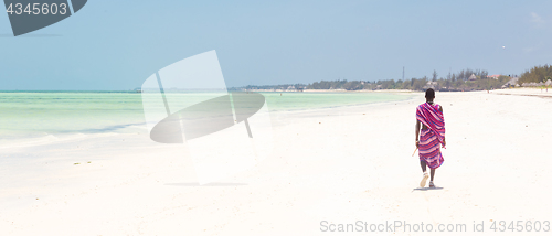 Image of Maasai warrior walking on picture perfect tropical sandy beach. Paje, Zanzibar, Tanzania.