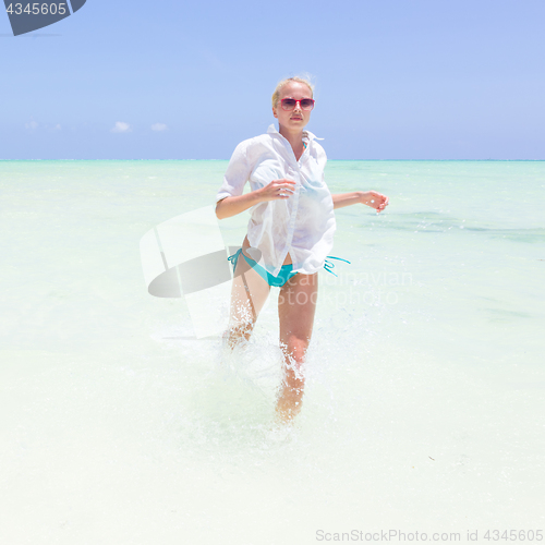 Image of Young active woman having fun running and splashing in shellow sea water.