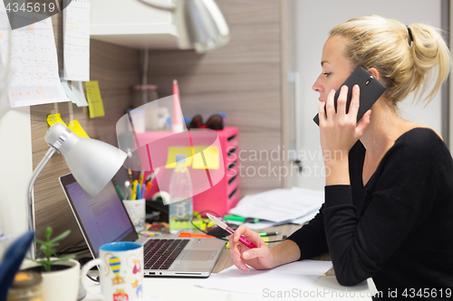 Image of Female entrepreneur talking on mobile phone in colorful modern creative working environment.