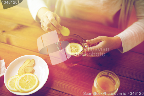 Image of close up of woman adding ginger to tea with lemon