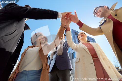 Image of group of happy people making high five in city