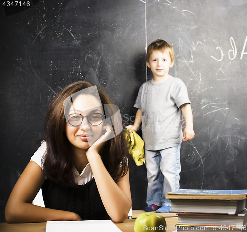 Image of little cute boy in glasses with young real teacher, classroom studying