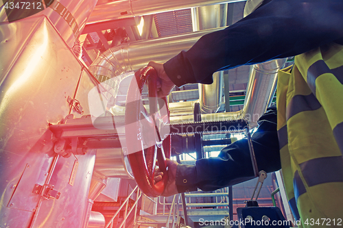 Image of industrial factory worker turning red wheel of valve