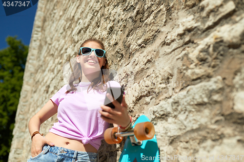 Image of happy teenage girl with longboard and smartphone